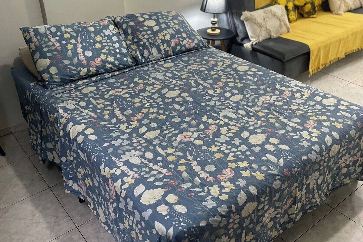 A bedroom with a large bed, a smaller sofa, a nightstand, and a lamp.