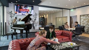 Una moderna zona relax con un pianoforte a coda, un divano in pelle rossa e un tavolo da scacchi.