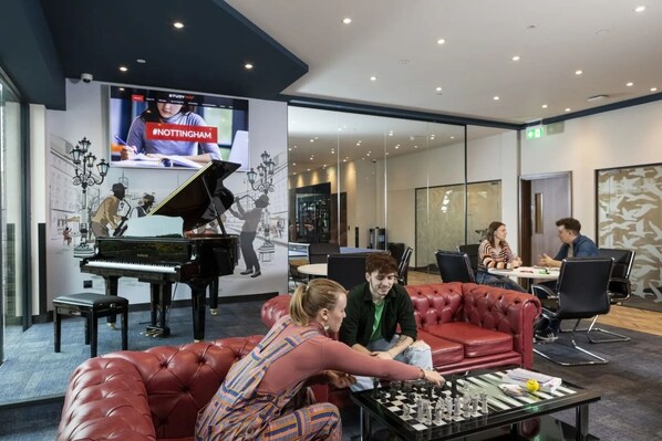 A modern lounge area with a grand piano, a red leather couch, and a chess table.
