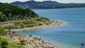 A beach with people and kayaks, surrounded by hills and trees.