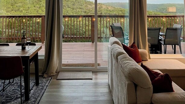A spacious room with a large window, a wooden deck, a sofa, and a dining table.