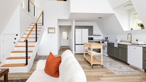A spacious loft apartment with a high ceiling, a wooden staircase, a kitchen with modern appliances, and a cozy seating area.