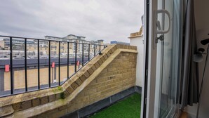 Un balcon avec un mur en briques et une porte vitrée, donnant sur un parking et des immeubles.