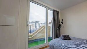 Une chambre avec une grande fenêtre, un lit avec une literie à rayures et une vue sur un immeuble doté d’un escalier.