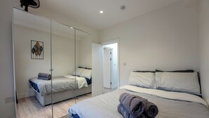 A bedroom with a large mirror, two beds, a wooden floor, and a door leading to another room. - Stylish and cozy flat (London)
