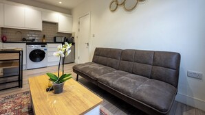 A modern living room with a sofa, a wooden coffee table with a plant, and a kitchen in the background. - Stylish and cozy flat (London)