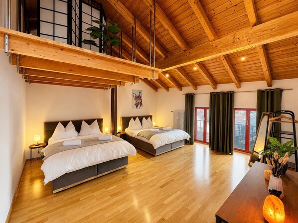 A spacious bedroom with two beds, wooden flooring, a sloped ceiling, and a large window.