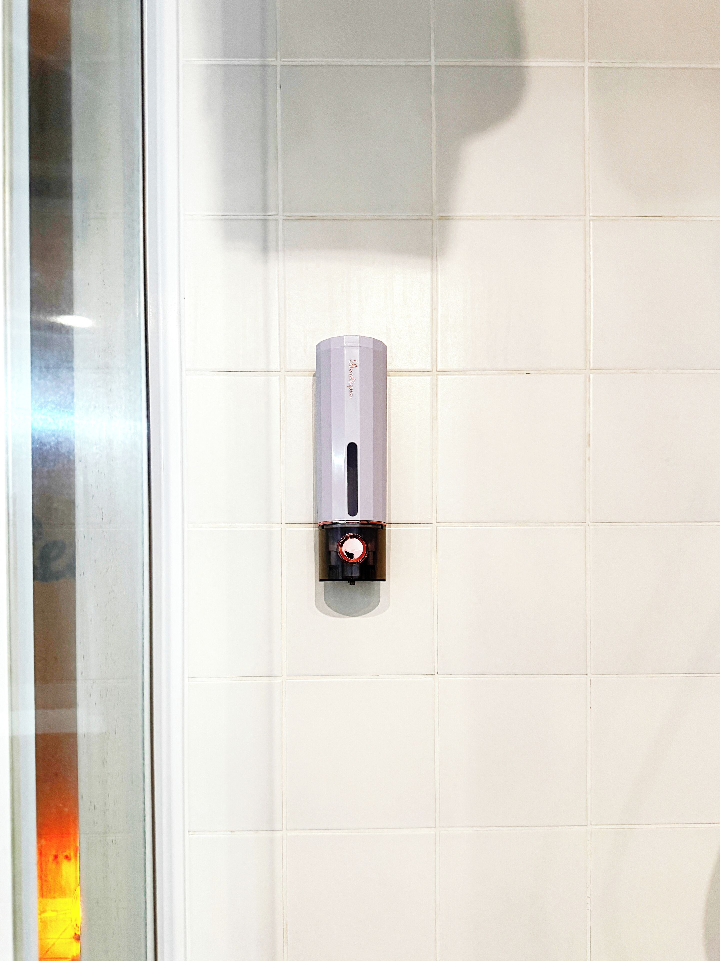 Un distributeur de gel hydroalcoolique fixé à un mur recouvert de carreaux blancs.