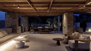 An outdoor patio area with stone pillars, wooden ceiling beams, and a variety of seating options including sofas, chairs, and tables. - Noero Villas Lefkada (Lefkada)