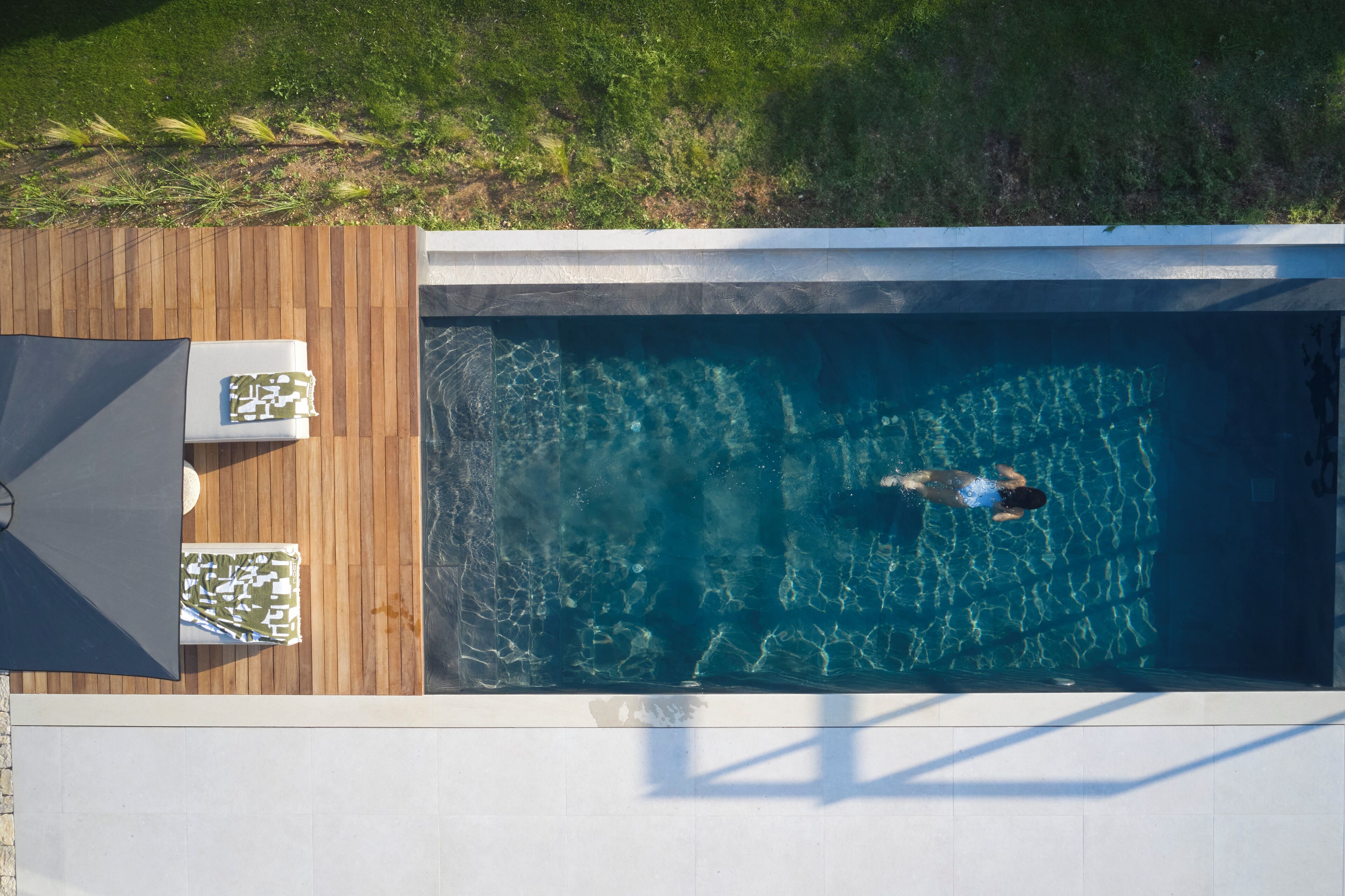 Piscina rectangular con muelle de madera y sillas de descanso, rodeada de césped.