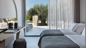 A modern hotel room with a large sliding glass door leading to an outdoor area, a bed with white linens, a small desk with a lamp, and a stone pillar. - Noero Villas Lefkada (Lefkada)