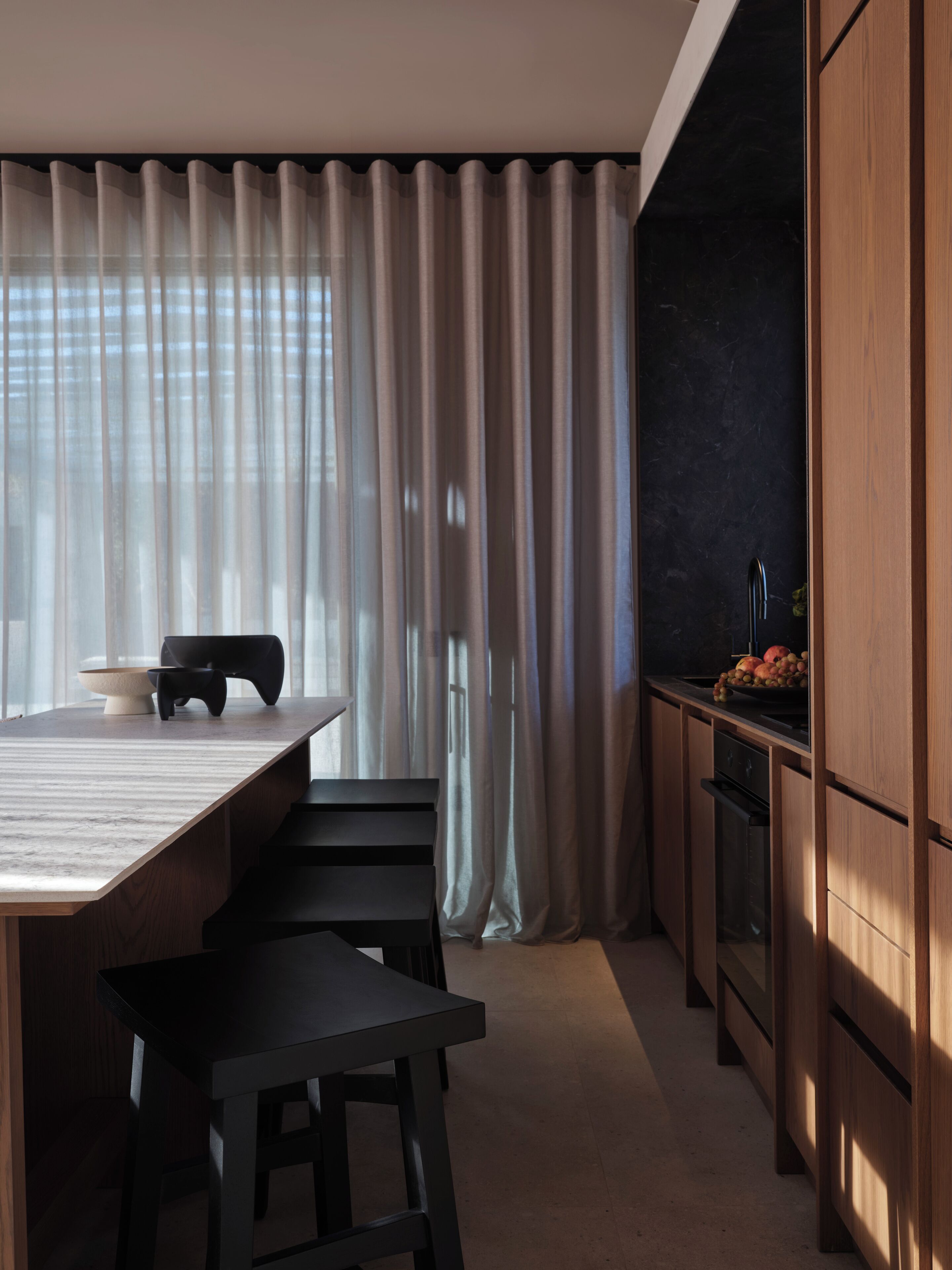 A modern kitchen with a wooden countertop, a dining area with a table and chairs, and a large window with sheer curtains.