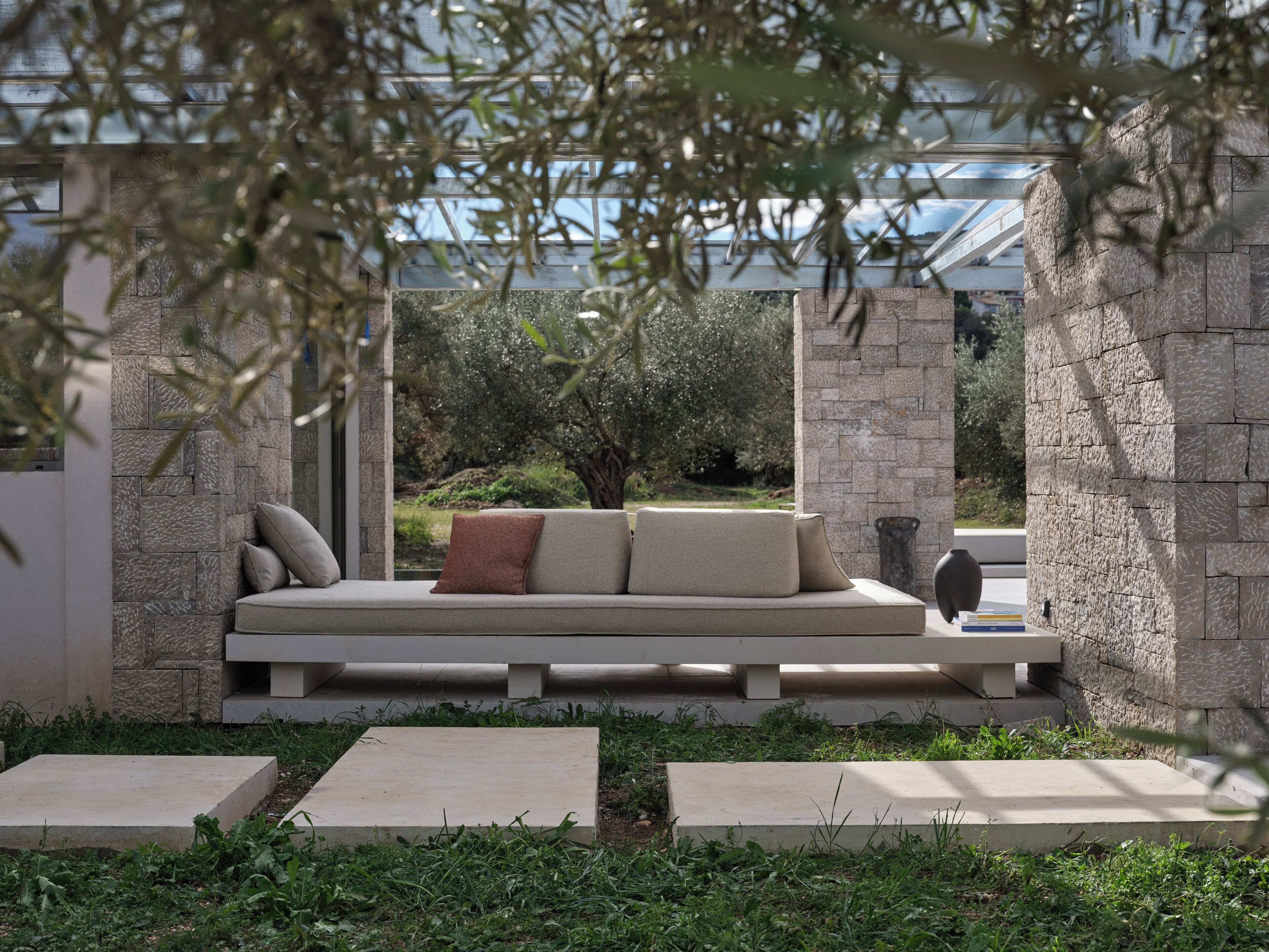 A modern outdoor seating area with a stone wall and a glass structure in the background.