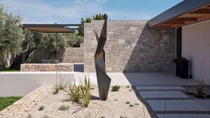 A modern outdoor patio with a stone wall, a metal sculpture, and a pergola. - Noero Villas Lefkada (Lefkada)