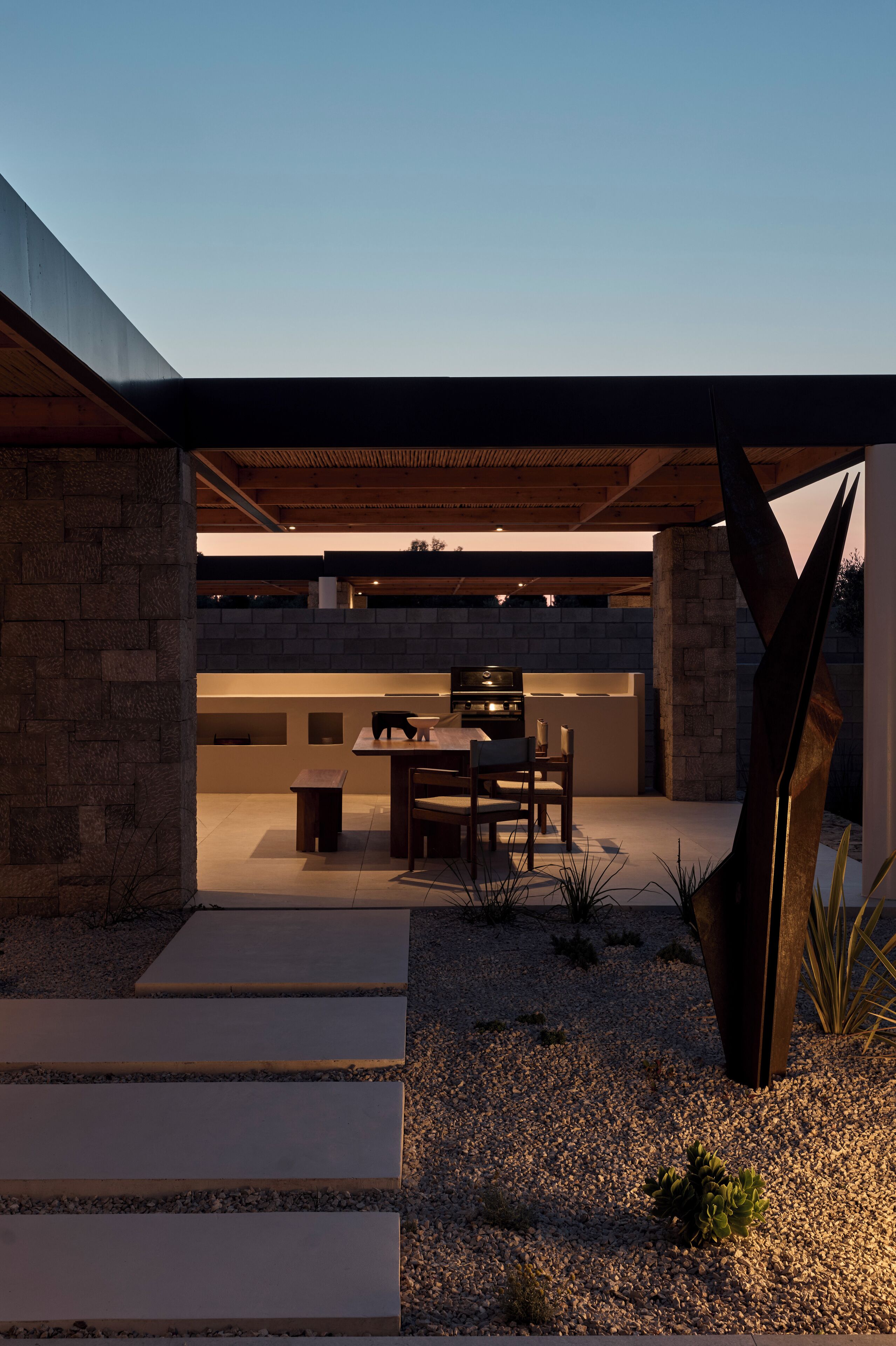A modern outdoor dining area with a stone wall, a wooden table, and chairs.