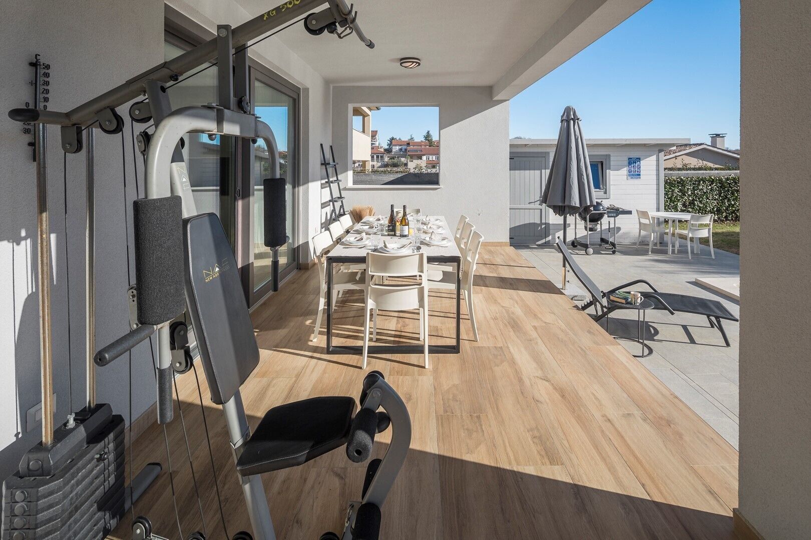 A modern home with a gym area, a dining area with a table set for four, and a patio with outdoor furniture.
