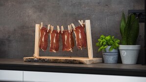 Un escurreplatos de madera con pinzas sujetando carne, una maceta con albahaca y una maceta con hojas anchas.