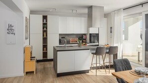 Una cocina moderna con armarios blancos, una isla central con taburetes y un comedor con mesa y sillas.