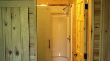 A wooden cabin bathroom with a shower, toilet, and a red mat.