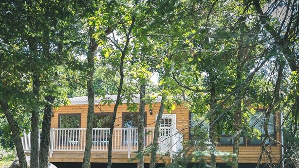 A wooden cabin with a deck and windows, surrounded by trees. - Pike's Place Cabin - Lakewood Park Cabins (Kenora, Unorganized)
