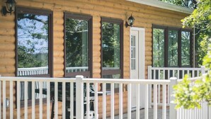 A log cabin with a porch, white railing, and large windows. - Pike's Place Cabin - Lakewood Park Cabins (Kenora, Unorganized)