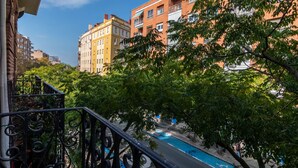 Un balcón con barandilla de hierro forjado que da a una piscina y edificios colindantes.