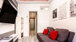 Una sala de estar moderna con un sofá gris, cojines rojos, un televisor de pantalla plana y suelo de madera.