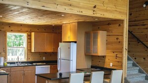 A modern kitchen with wooden walls, a refrigerator, a sink, and a bar area with chairs.