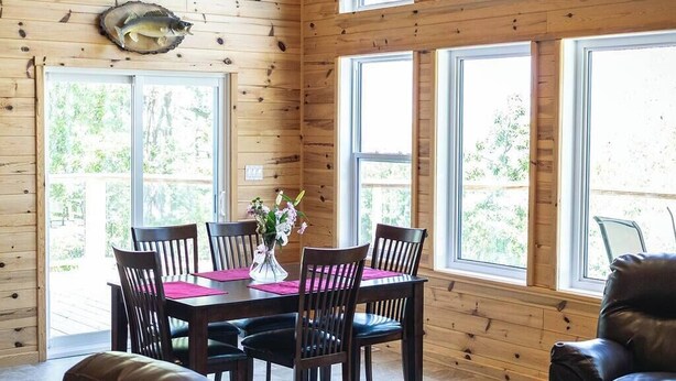 A wooden-paneled room with a dining table set for four, large windows, and a fish mounted on the wall.