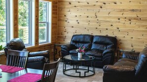 A cozy room with a wooden wall, a leather sofa, a dining table with chairs, and a small round table with a vase of flowers.