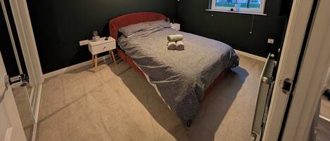 A bedroom with a bed, bedside table, and a window with blinds.