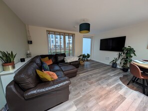 A modern living room with a leather sofa, a dining table, and potted plants. - Petfriendly 1bedapt - 5 Min From Beach Aberdeen (Aberdeen)