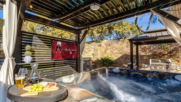 An outdoor hot tub area with a table set for a meal, a wine glass, and a pitcher. - Hot Tub + Games + Mini Golf | Open Labor Day! (Canyon Lake)