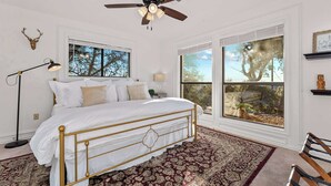 A bedroom with a bed, a ceiling fan, a large window, and a view of trees. - Hot Tub + Games + Mini Golf | Open Labor Day! (Canyon Lake)