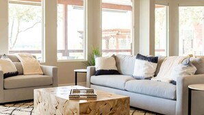 A living room with two sofas, a coffee table, and large windows with a view of buildings and trees. - Lake Views, Fire Pit, BBQ & Patio | Pet-Friendly! (Canyon Lake)