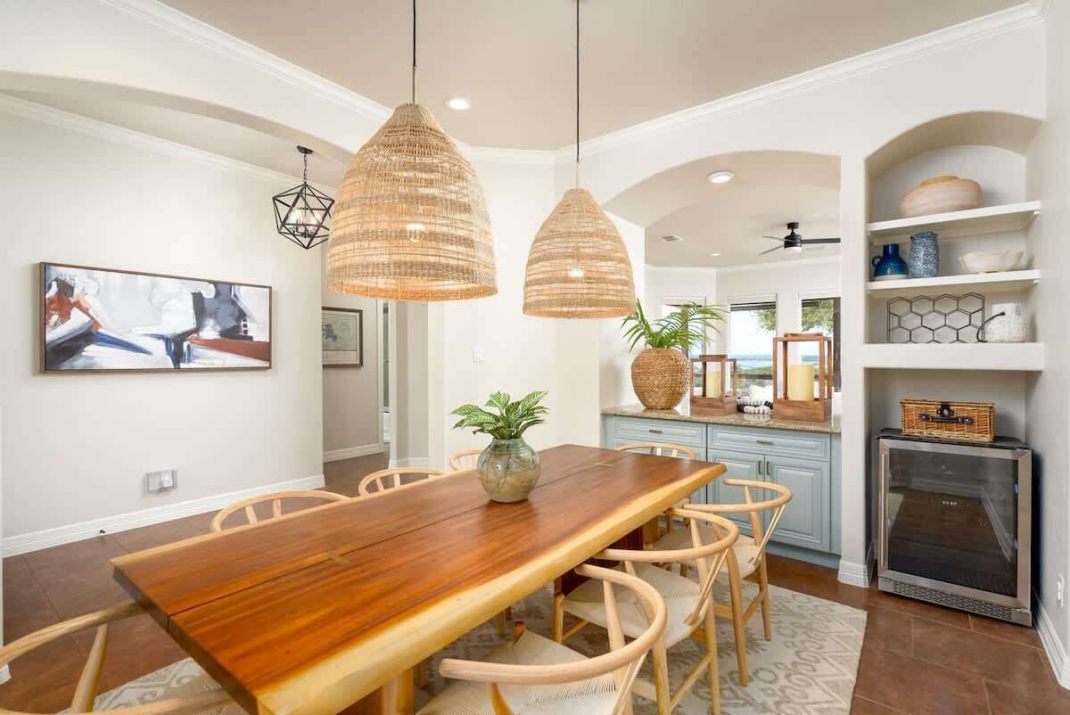 Un espace repas avec une table et des chaises en bois, des luminaires suspendus et une cuisine en arrière-plan.