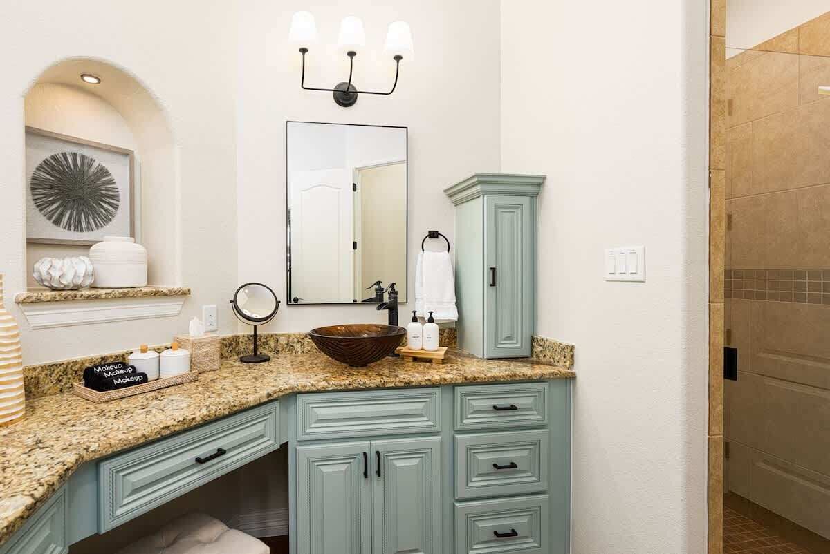A bathroom with a granite countertop, a large mirror, a vanity with drawers, a sink with a vessel basin, and a light fixture above the mirror.