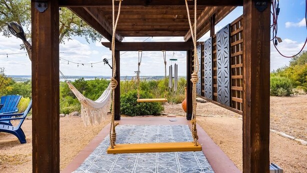 A wooden pergola with a hammock and swing set, a blue chair, and a view of the landscape. - Lake Views, Fire Pit, BBQ & Patio | Pet-Friendly! (Canyon Lake)