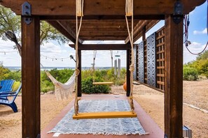 Una pérgola de madera con hamaca y columpio, una silla azul y vistas al paisaje.