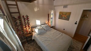 A bedroom with a bed, a nightstand, a ladder, a window with curtains, and a painting on the wall. - cozy lakeside retreat (Silver springs)