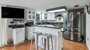 A modern kitchen with white cabinets, a stainless steel refrigerator, and a large island with stools. - cozy lakeside retreat (Silver springs)