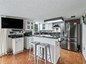 A modern kitchen with white cabinets, a stainless steel refrigerator, and a large island with stools.