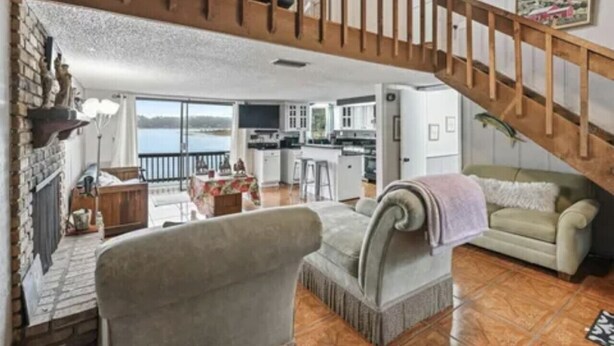 A spacious living area with a wooden staircase, a kitchen, and a balcony with a view. - cozy lakeside retreat (Silver springs)
