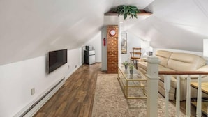 A modern loft with a wooden floor, a beige sofa, a TV mounted on the wall, and a brick accent wall.