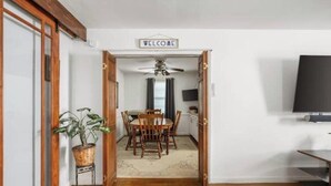 A hallway with a wooden floor leading to a dining area with a table and chairs, a ceiling fan, and a 'WELCOME' sign.