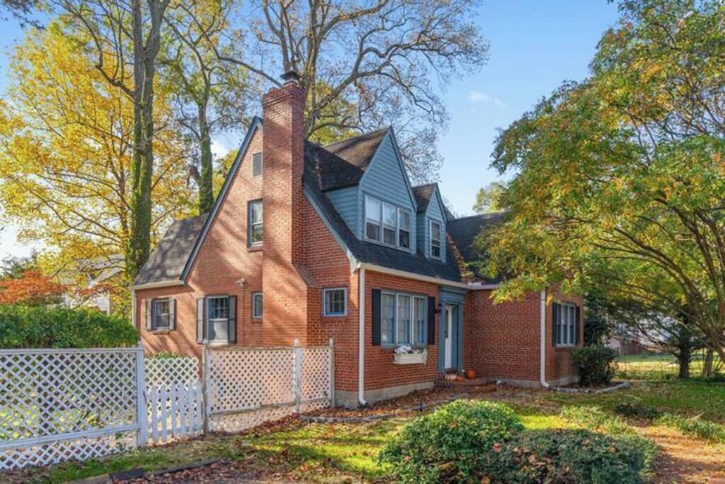 Una casa de ladrillo de dos pisos con techo a dos aguas y cerca de piquetes blancos.