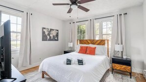 Quarto com cama, ventilador de teto, televisão e janela com cortinas.