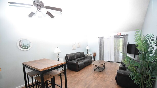 A living room with a wooden table, black leather sofa, and a ceiling fan. - Nice 2 Bedroom Duplex Great For Contractors (Saint Mary's)