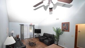 A living room with a ceiling fan, a flat-screen TV, a black leather sofa, a wooden coffee table, and a potted plant. - Nice 2 Bedroom Duplex Great For Contractors (Saint Mary's)