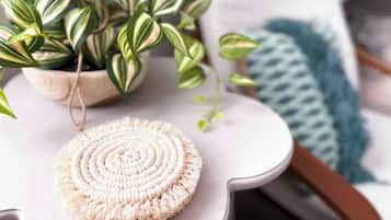 A round, textured mat on a white table with a plant and a blue knitted item in the background.
